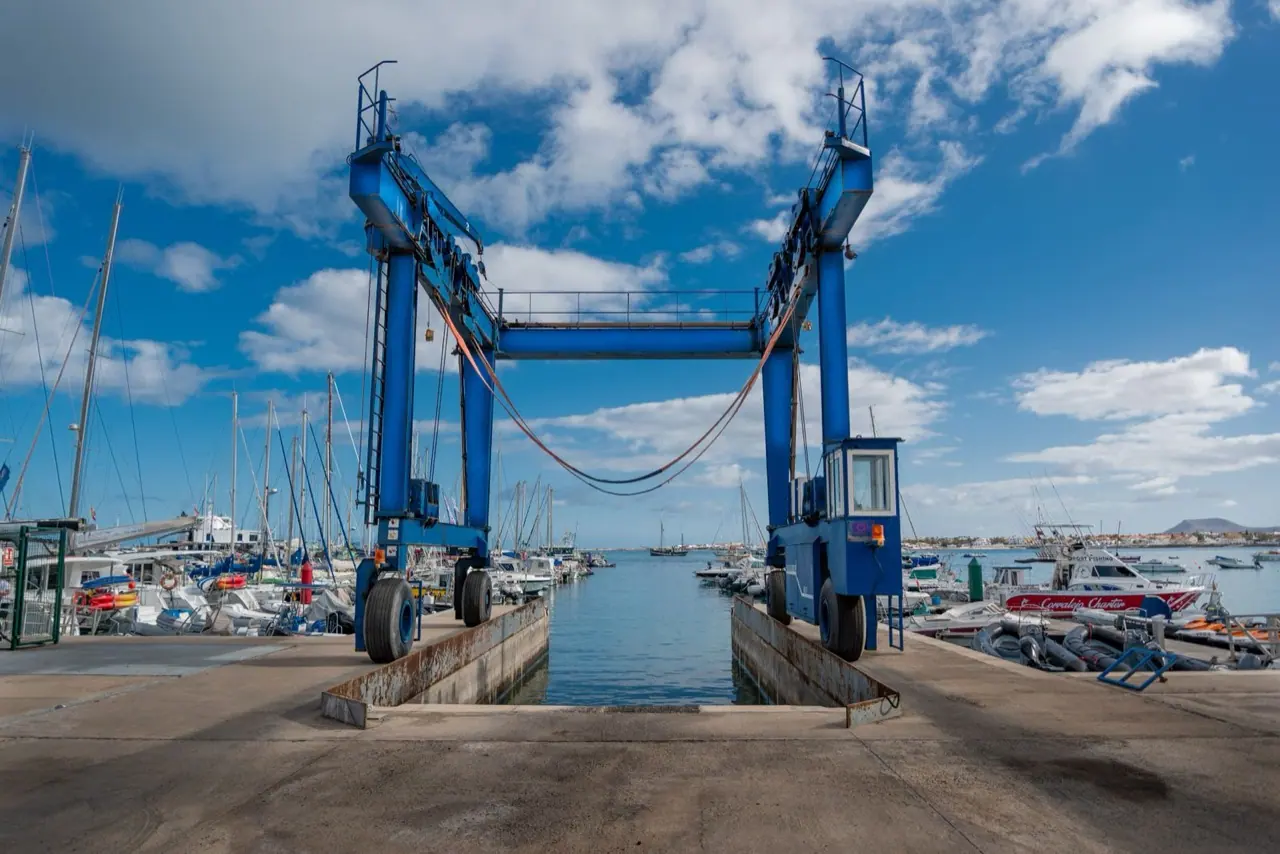 A blue travel lift with slings at a marina haul-out well